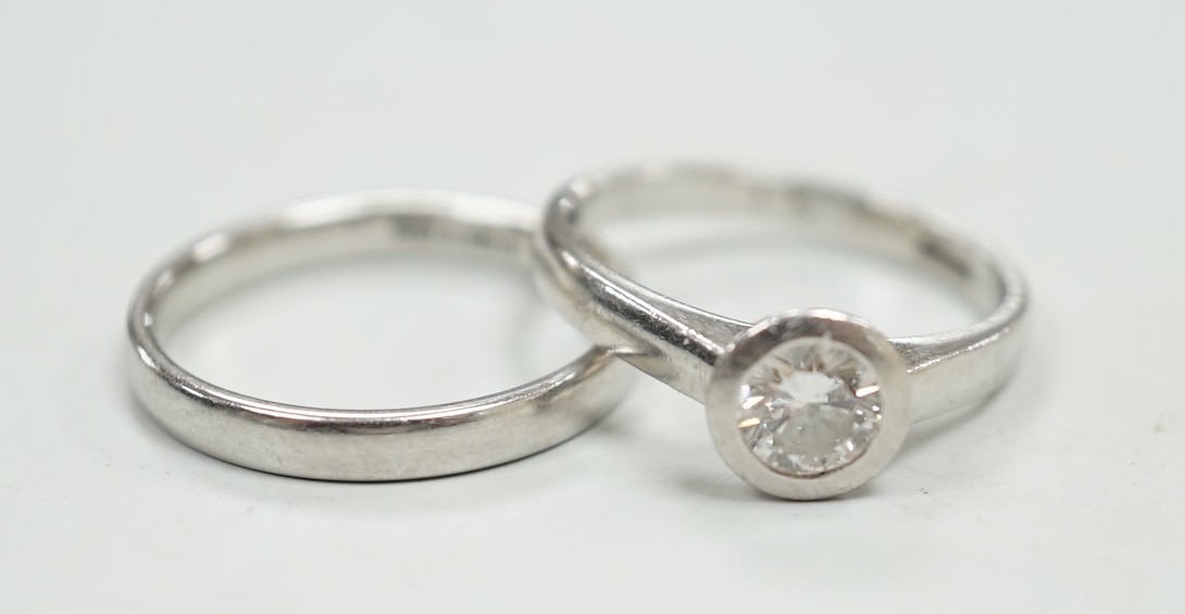 A modern platinum and collet set solitaire diamond ring, size M, gross weight 4.9 grams, together with a modern platinum wedding band, size N, 3.8 grams.